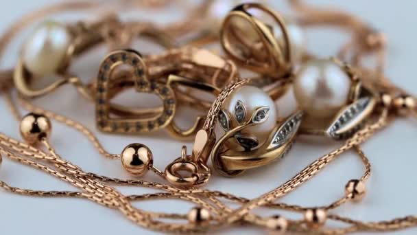 Złote kolczyki i pierścienie z kamieniami szlachetnymi i perłami obracają się na białej powierzchni — Wideo stockowe