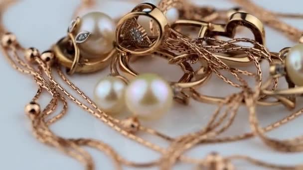 Złote kolczyki i pierścienie z kamieniami szlachetnymi i perłami obracają się na białej powierzchni — Wideo stockowe