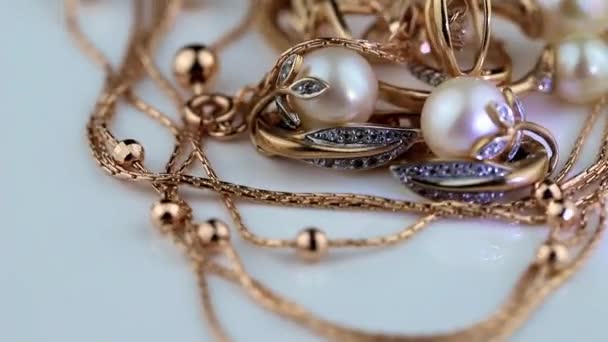 Boucles d'oreilles et bagues en or avec pierres précieuses et perles tournent sur une surface blanche — Video