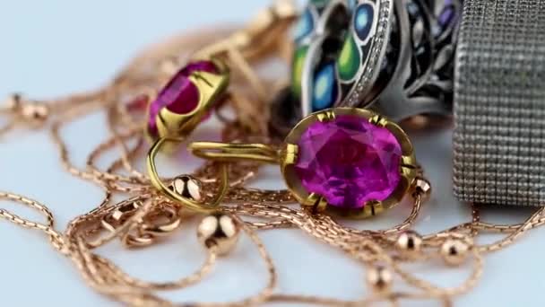 Pendientes de oro con grandes rubíes rojos, anillos, cadena y colgante giran sobre una superficie blanca — Vídeo de stock