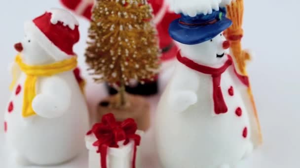 Spielzeugfiguren eines Schneemanns, Weihnachtsmänner und Weihnachtsbäume rotieren auf weißer Fläche — Stockvideo