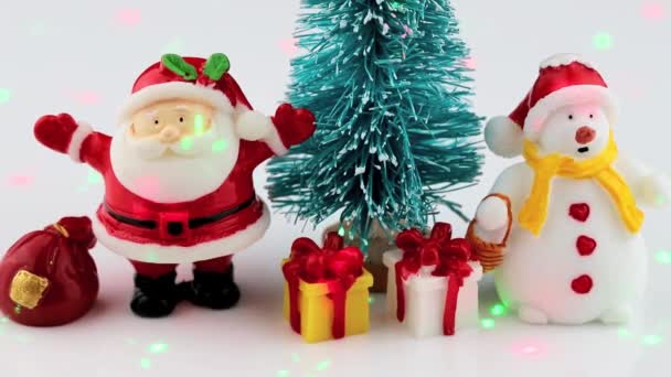Spielzeugfiguren eines Schneemanns, Weihnachtsmänner und Weihnachtsbäume werden von farbigen Laserstrahlen beleuchtet — Stockvideo