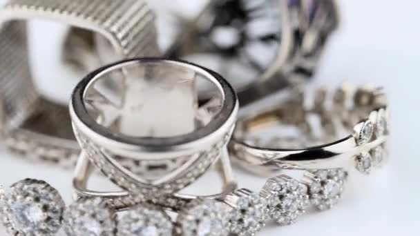 Anillos de plata de varias formas con diferentes gemas giran sobre una superficie blanca — Vídeos de Stock