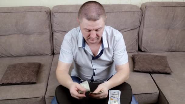 Um homem de meia-idade sentado no sofá conta seu dinheiro — Vídeo de Stock