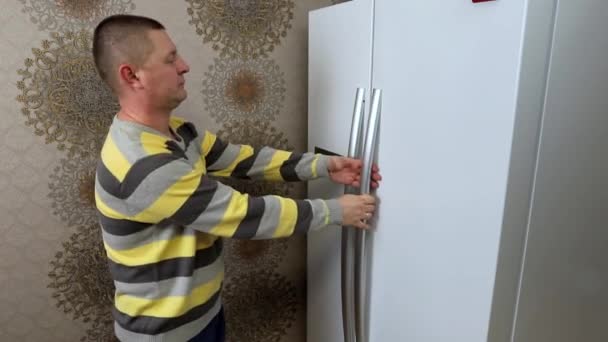 Egy férfi kinyitja a hűtő ajtaját a konyhában, és örömmel táncol.. — Stock videók