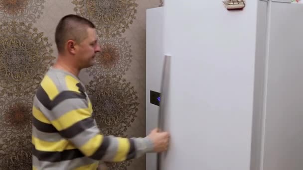 Мужчина открывает холодильник на кухне и берет спелый мандарин оттуда. — стоковое видео