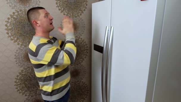 Человек молится перед холодильником, чтобы в нем была вкусная еда. — стоковое видео