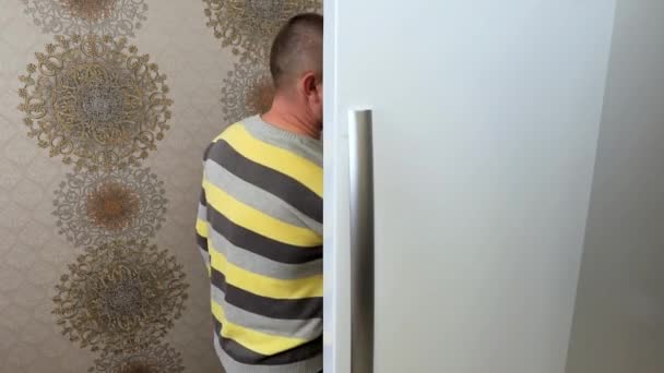 Egy férfi kinyitja a hűtőt a konyhában, és iszik onnan egy pohár gyümölcslevet.. — Stock videók