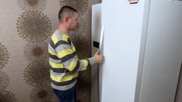 Um homem abre a geladeira na cozinha e escolhe por um longo tempo que comida levar — Vídeo de Stock