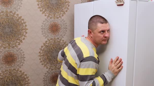 Muž v pruhovaném svetru poslouchá, co se děje v ledničce. — Stock video