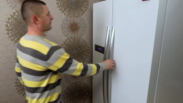 Мужчина берет бутылку молока из кухонного холодильника — стоковое видео