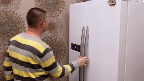 Мужчина берет бутылку молока из кухонного холодильника — стоковое видео