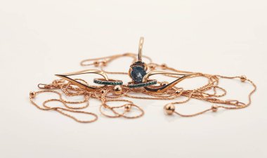 Zümrüt şeklinde altın küpeler ince altın bir kolye ile çevrili.