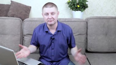 Oturma odasındaki koltukta oturan mavi gömlekli bir adam seyirciyi jestleriyle blogunu izlemeye davet ediyor..