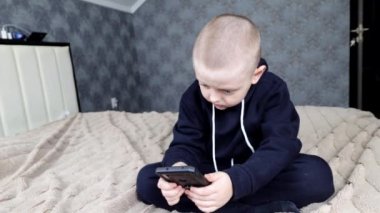 Mavi kapüşonlu anaokulu çocuğu akıllı telefona bakıyor.