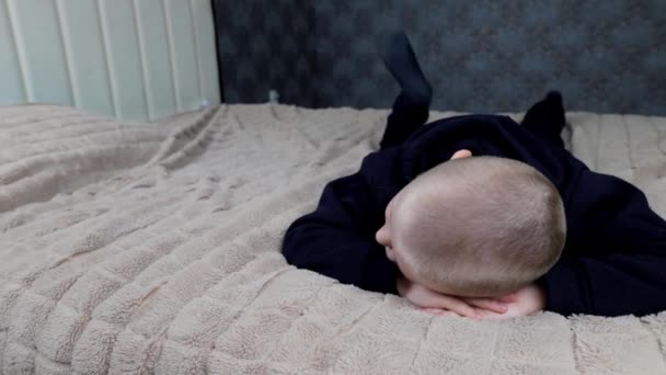 Ένα νήπιο ξαπλώνει στο κρεβάτι και φλυαρεί με τα πόδια του — Αρχείο Βίντεο