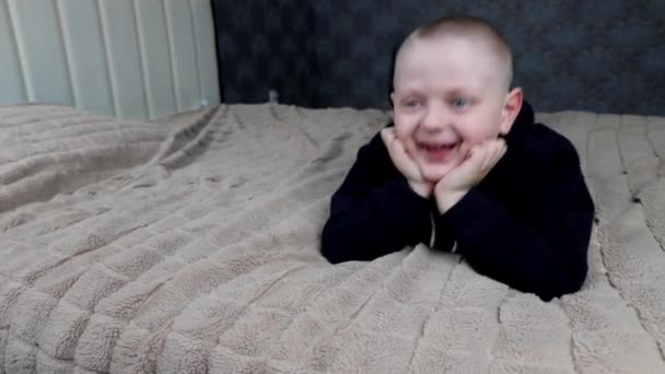 Un bambino in età prescolare si sdraia sul letto e chiacchiera con i piedi — Video Stock