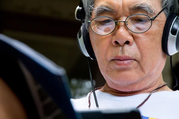 Hombre mayor relajándose en casa leyendo E-book en su tableta — Foto de Stock