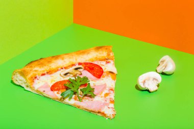 Yeşil ve turuncu arka planda jambonlu ve mantarlı pizza.