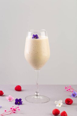 Meyveli ve çiçekli bardakta beyaz milkshake kokteyli