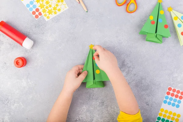 Το παιδί διακοσμεί το origami δέντρο χαρτί. Χριστουγεννιάτικο κολάζ. Φτιαγμένο με τα ίδια του τα χέρια. Παιδική τέχνη έργο τέχνης για τα παιδιά. Χειροτεχνία για παιδιά. Άνω όψη — Φωτογραφία Αρχείου