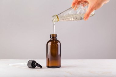 Kadın eliyle duş jelini yeniden kullanılabilir cam şişeye dolduruyor.