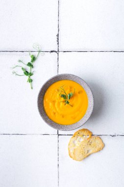 Beyaz fayanslı balkabağı ve havuç kremalı çorba ve kızarmış ekmek. Üst görünüm.