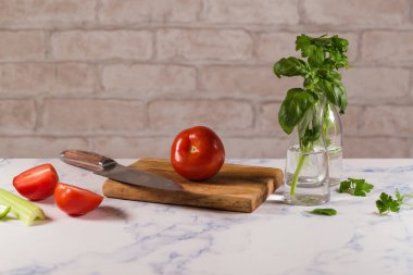 Kadınların elleri beyaz önlüklü, siyah eldivenli yeşil tahtada, taze sebzelerin arkasında domates kesiyor..