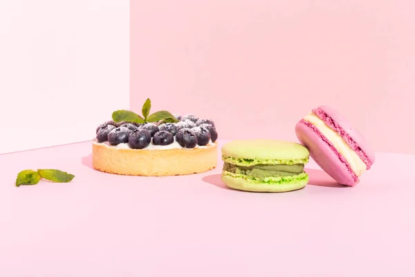 Primer plano de tartas de postre de arándanos frescos gourmet de lujo y macarrones franceses en rosa — Foto de Stock