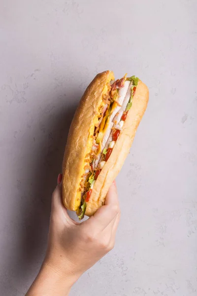 Main de femme tient sandwich sur mur gris ombres dures. Concept de promotion sandwich — Photo