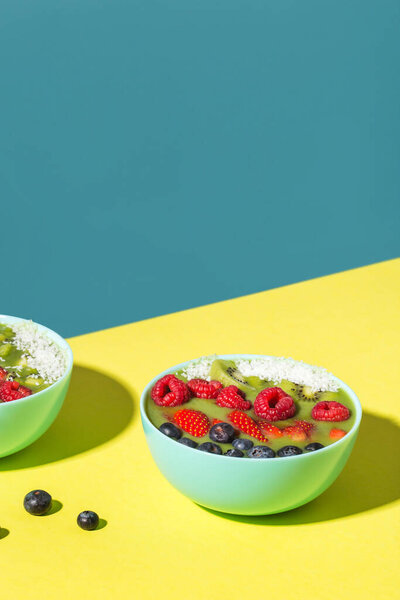 smoothie bowl with fresh berries and fruits in blue plate on yellow dark shadow