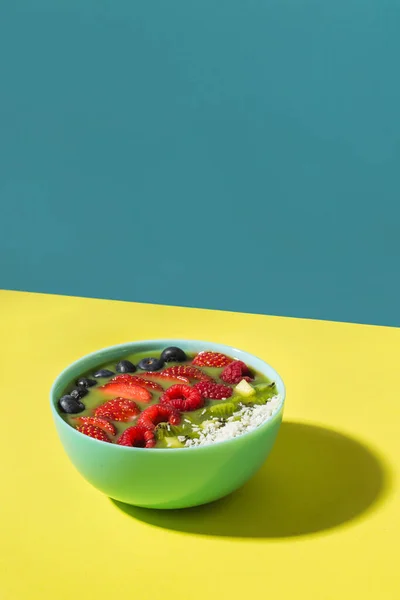 Tazón de batido con bayas frescas y frutas en plato azul en la sombra amarilla oscura Imágenes De Stock Sin Royalties Gratis