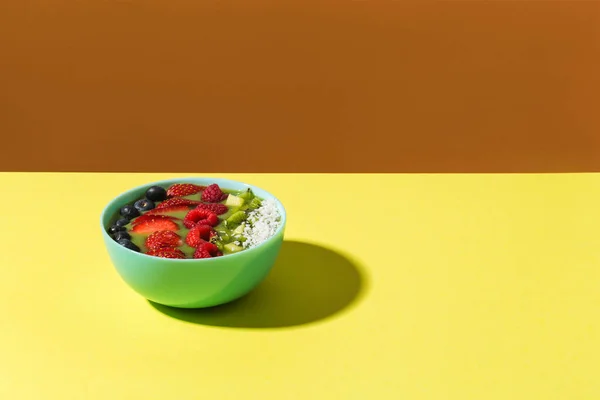 Чаша смузи со свежими ягодами и фруктами в голубой тарелке на желтой темной тени Лицензионные Стоковые Изображения