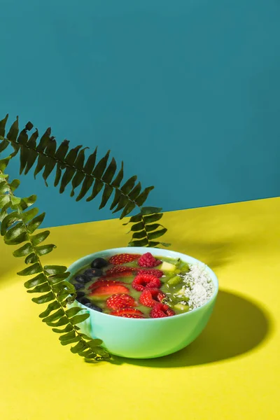 Tazón de batido con bayas frescas y frutas en plato azul en la sombra amarilla oscura Fotos De Stock