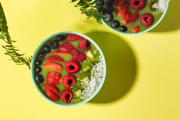 Чаша смузи со свежими ягодами и фруктами в голубой тарелке на желтой темной тени Лицензионные Стоковые Фото