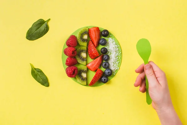 Smoothie tál friss bogyók és gyümölcsök papír kézműves tányéron sárga gyermek kéz egészséges étel koncepció Stock Kép