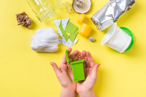 Pequeño cubo de basura en manos de niños. Papel de basura limpio, plástico, metal, vidrio. Concepto de reciclaje en amarillo. Fotos De Stock