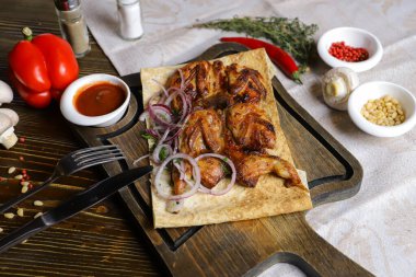 Koyu bir tezgahın üzerinde, açık keten bir peçete, bir kesme tahtası üzerinde dört bıldırcın kızarttı kırmızı soğan halkalarıyla birlikte pita ekmeğinde, keten peçetede, kırmızı biber, biberiye dalında.