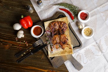 Koyu bir tezgahın üzerinde, açık keten bir peçete, bir kesme tahtası üzerinde dört bıldırcın kızarttı kırmızı soğan halkalarıyla birlikte pita ekmeğinde, keten peçetede, kırmızı biber, biberiye dalında.