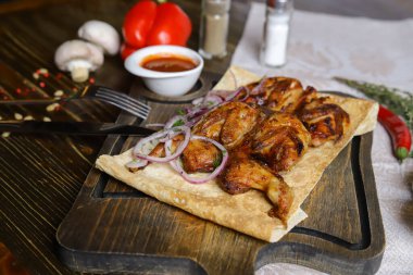 Koyu bir tezgahın üzerinde, açık keten bir peçete, bir kesme tahtası üzerinde dört bıldırcın kızarttı kırmızı soğan halkalarıyla birlikte pita ekmeğinde, keten peçetede, kırmızı biber, biberiye dalında.