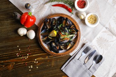 Bir dilim limon, çatal bıçak, kırmızı biber, acı kırmızı biber, beyaz mantar ve bir dal biberiye ile servis edilen midyeler..