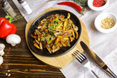 Kızartma tavasında, sosta, çatal bıçakta, kırmızı biberde, şampiyonlarda, sosta, acı biberde, baharatlarda, biberiyede pişirilmiş et parçaları masada. Kızarmış patates kızartma tavasında servis edilir.