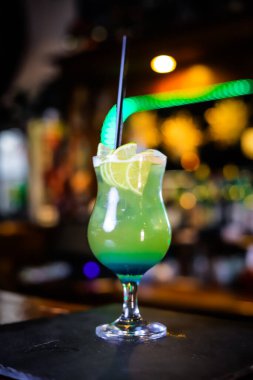 Uzun yeşil bardakta bir kokteyl, limon dilimleri ve siyah bir pipet.. 
