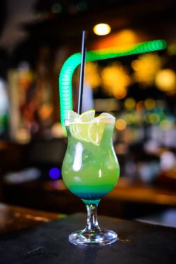 Uzun yeşil bardakta bir kokteyl, limon dilimleri ve siyah bir pipet.. 