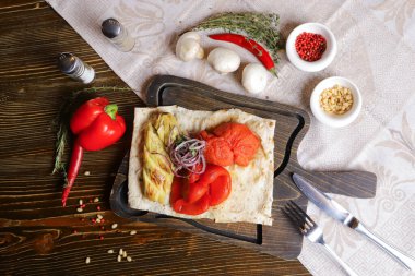 Pita ekmeği ızgara sebze kabağı, kırmızı biber, koyu renk kesim tahtasında derisiz domates, siyah masa üstünde keten peçete ile servis edilir. Bir çift biber ve tuz, çatal bıçak takımı, beyaz mantar, bütün kırmızı biber, acı biber, ro