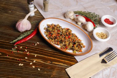 Koyu bir tezgahta Pilaf oval bir tabakta, siyah pirinçli pilav, keten tohumu salatası, çatal bıçak, tuz ve biber, baharat ile servis edilir.