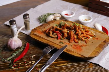 Acı soslu ve baharatlı deniz ürünleri mürekkep balığı. Koyu bir masanın üstünde, çatal bıçak takımı, bir baş sarımsak, beyaz şampiyon, bir çift biber ve tuz, bir biberiye dalı..