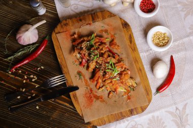 Acı soslu ve baharatlı deniz ürünleri mürekkep balığı. Koyu bir masanın üstünde, çatal bıçak takımı, bir baş sarımsak, beyaz şampiyon, bir çift biber ve tuz, bir biberiye dalı..