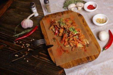 Acı soslu ve baharatlı deniz ürünleri mürekkep balığı. Koyu bir masanın üstünde, çatal bıçak takımı, bir baş sarımsak, beyaz şampiyon, bir çift biber ve tuz, bir biberiye dalı..