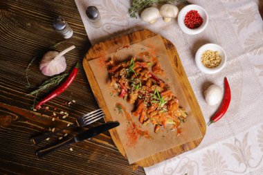 Acı soslu ve baharatlı deniz ürünleri mürekkep balığı. Koyu bir masanın üstünde, çatal bıçak takımı, bir baş sarımsak, beyaz şampiyon, bir çift biber ve tuz, bir biberiye dalı..